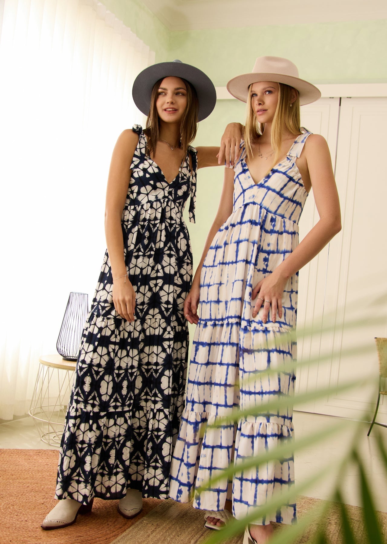 Mujeres en sala con vestidos largos blanco con azul y negro con blanco y sombreros.