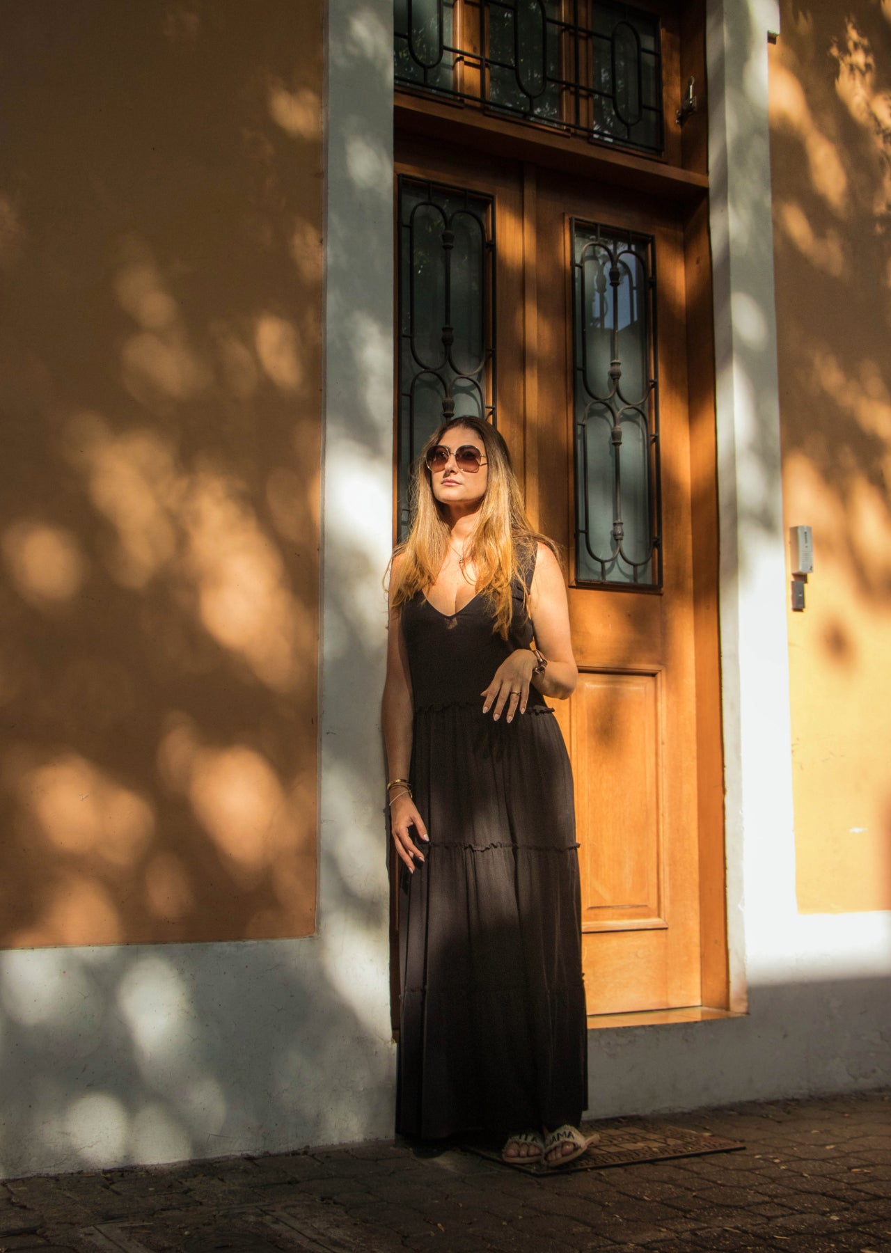 Mujer posando junto a puerta de madera con vestido largo color negro.
